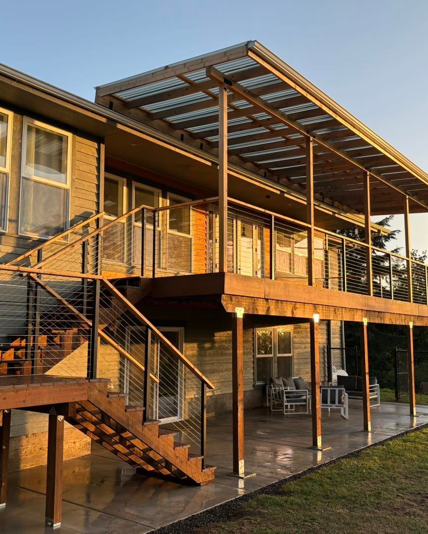 Multi-level wooden deck with stairs attached to a house with a corrugated roof in the evening light.