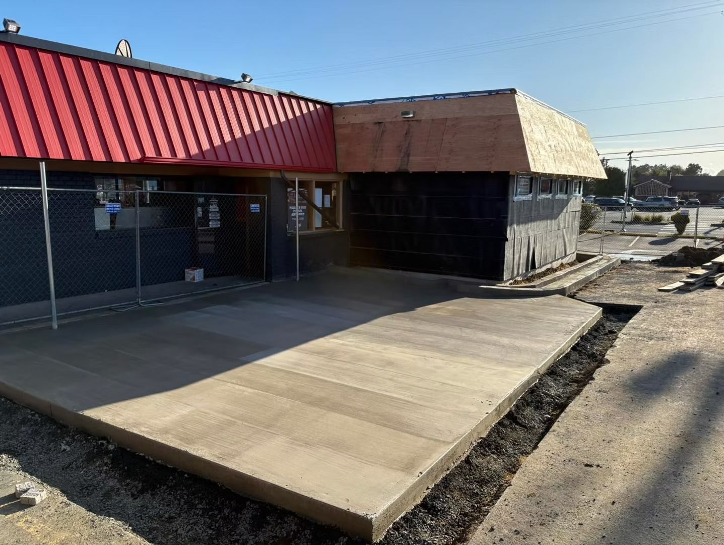Exterior of a building under construction. Red roof, exposed plywood, fresh concrete, asphalt road.