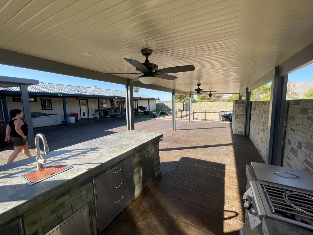 Covered outdoor kitchen with stone accents, ceiling fans, and a person walking in the background.