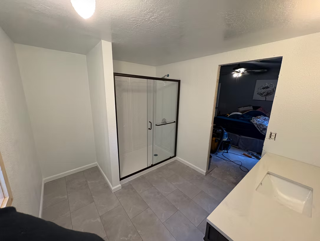 Bathroom interior with shower, vanity, gray tile floor, and a doorway.