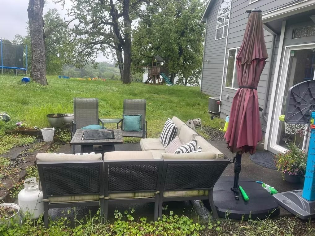 Outdoor seating area with a sofa, chairs, and umbrella on a grassy lawn.