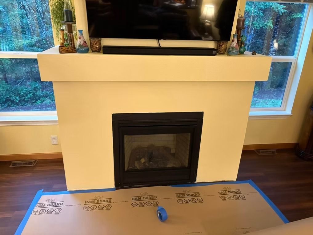 Cream-colored fireplace with a black firebox, a TV above it, and brown flooring.