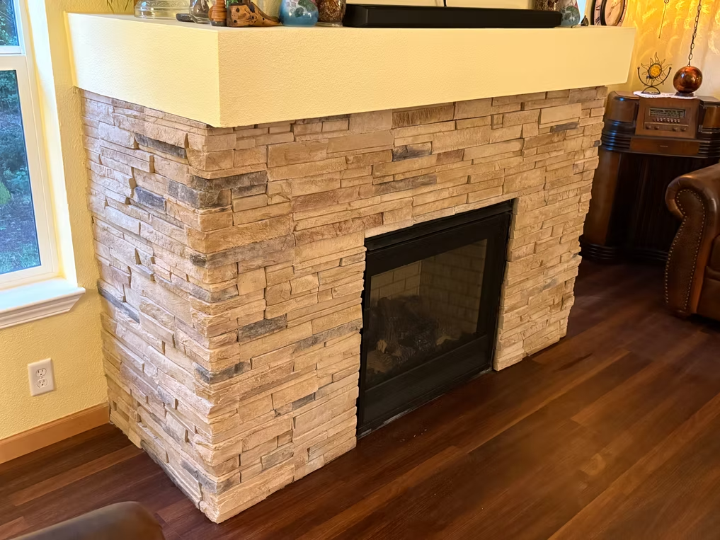 Fireplace with stacked stone facade and cream-colored mantle. Black firebox is open.