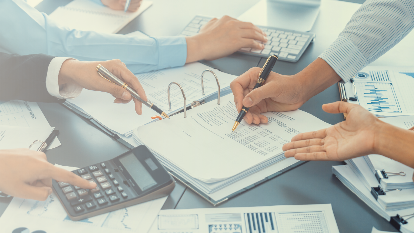 Hands working on paperwork, using calculator, and typing on a keyboard, suggesting financial or accounting work.