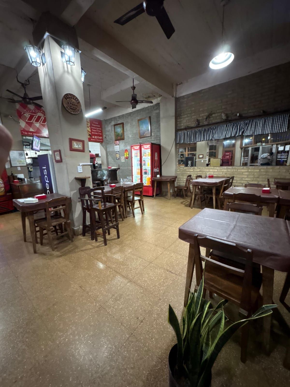 Vista interior de un restaurante con mesas y sillas de madera, máquina de bebidas y decoración vintage.