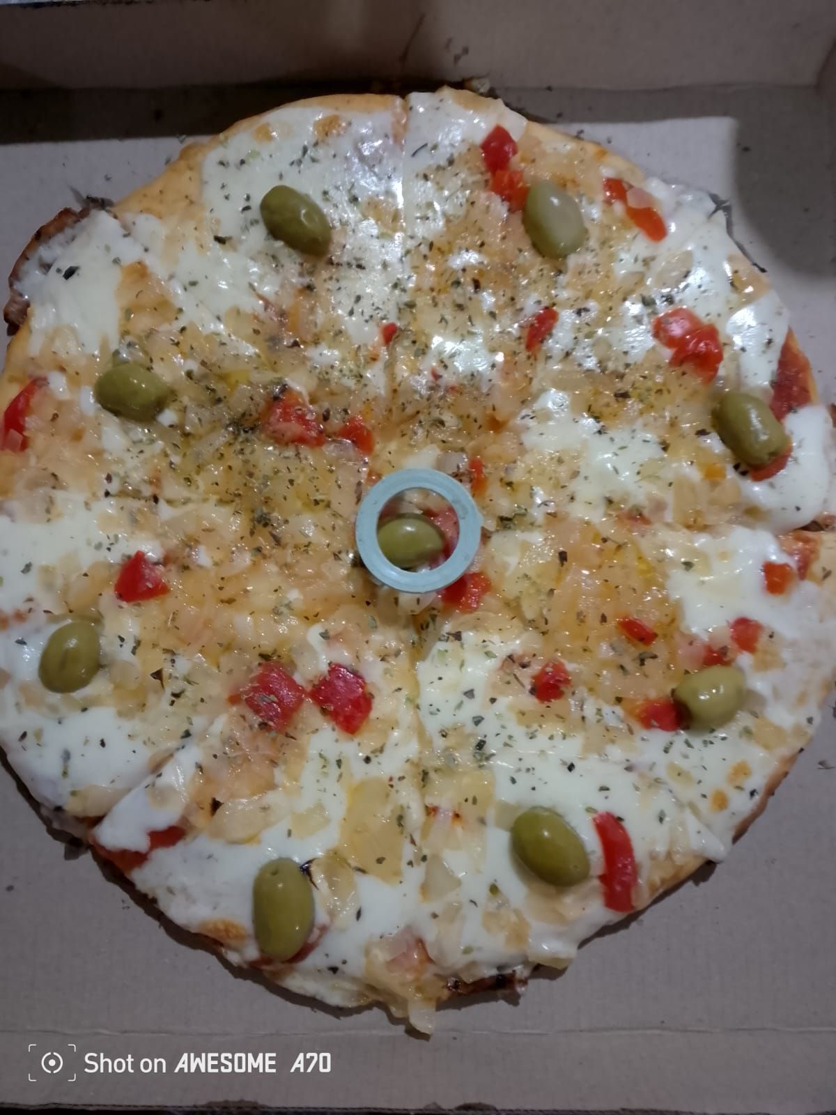 Pizza con aceitunas, pimientos rojos y cebollas, dentro de una caja de cartón.