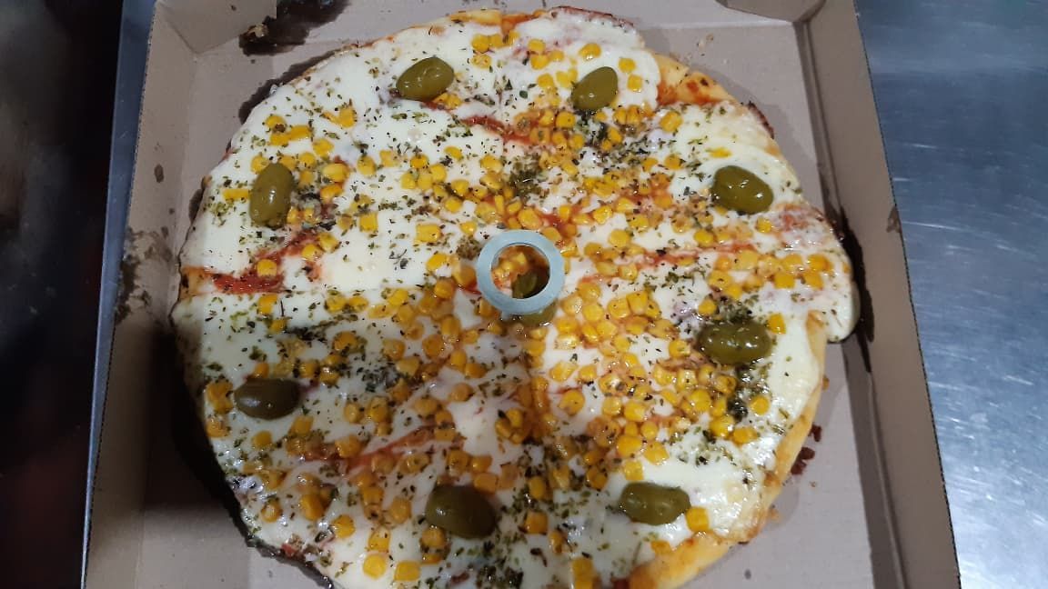 Pizza con queso, maíz, aceitunas y hierbas en caja de cartón.