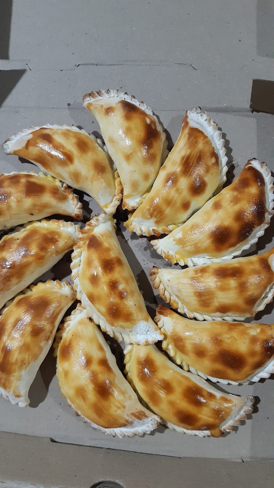 Empanadas doradas dispuestas en forma de círculo, horneadas con una corteza rizada, colocadas en un recipiente de cartón.