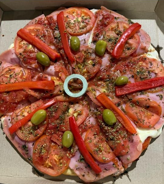 Pizza con tomates, jamón, pimientos, aceitunas y hierbas en una caja de cartón.