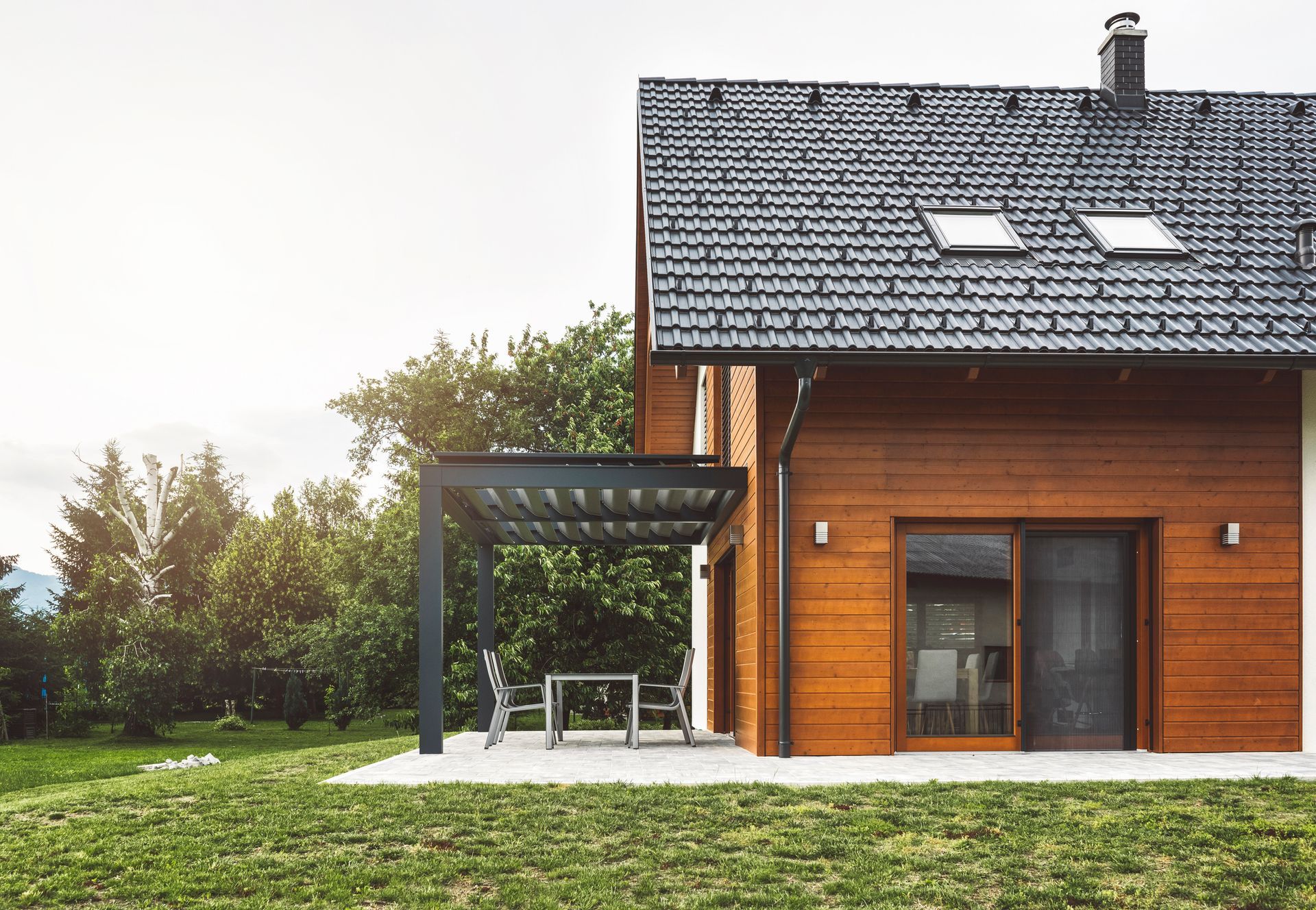 A wooden house with a slate roof and a pergola in the backyard.