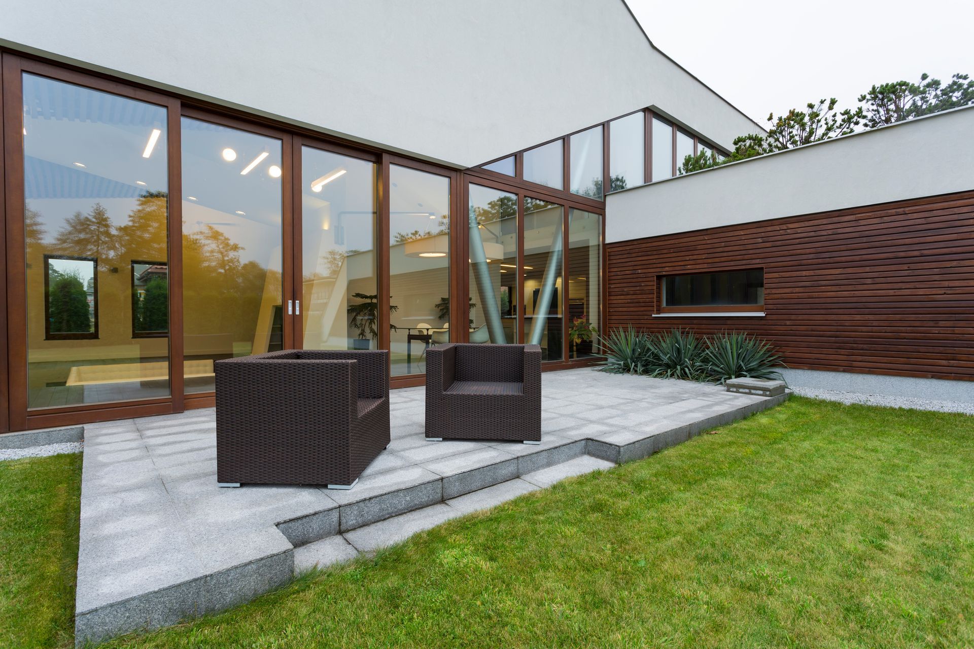 A patio with chairs and a table in front of a house with a lot of windows.