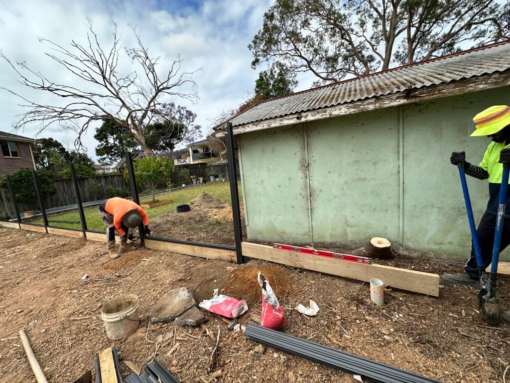 Two men are working on a fence in front of a building.