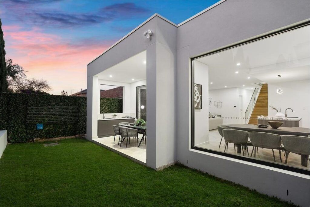 A white house with a large window and a large lawn in front of it.
