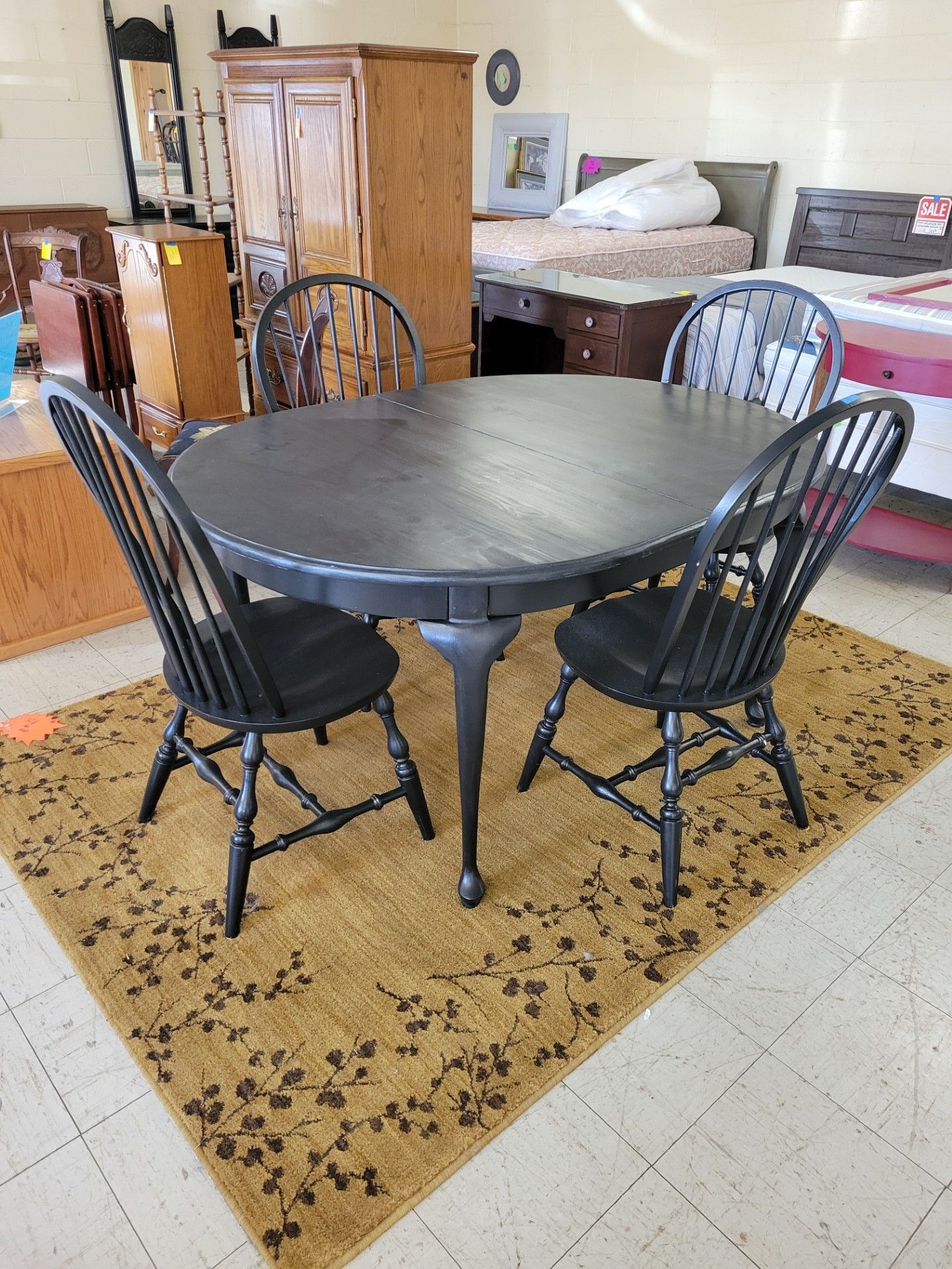 Black round dining table with four matching chairs on a floral rug. In a furniture store.