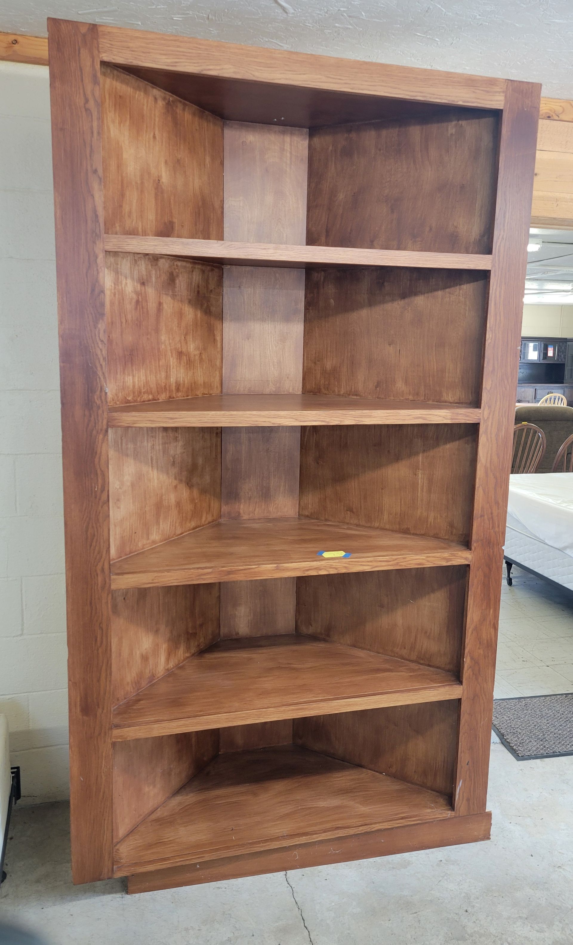 A wooden corner bookshelf is sitting on the floor in a room - Mountain Home, AR - Chuck's Outlet & Moving Inc