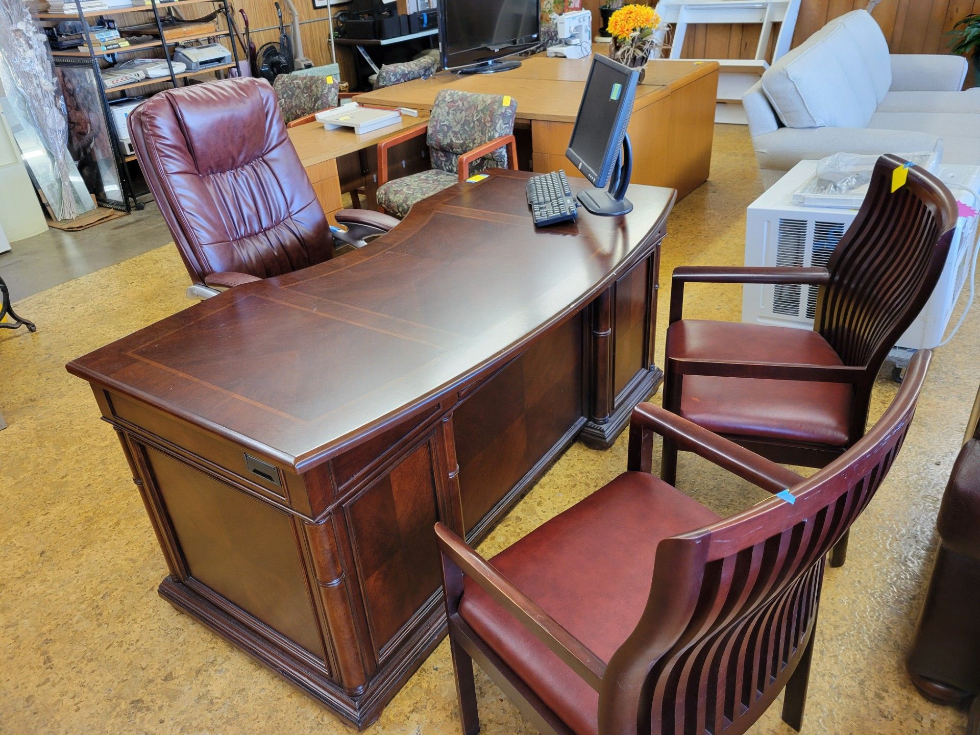 Dark wood office desk with a leather chair, two side chairs, and a computer.