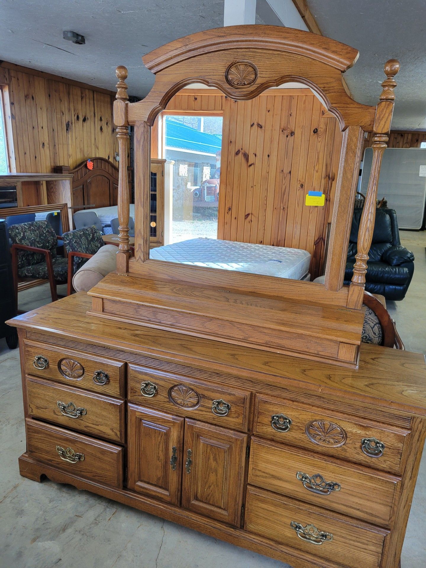 Wooden dresser with attached mirror, brown with decorative carvings, in a room with other furniture.