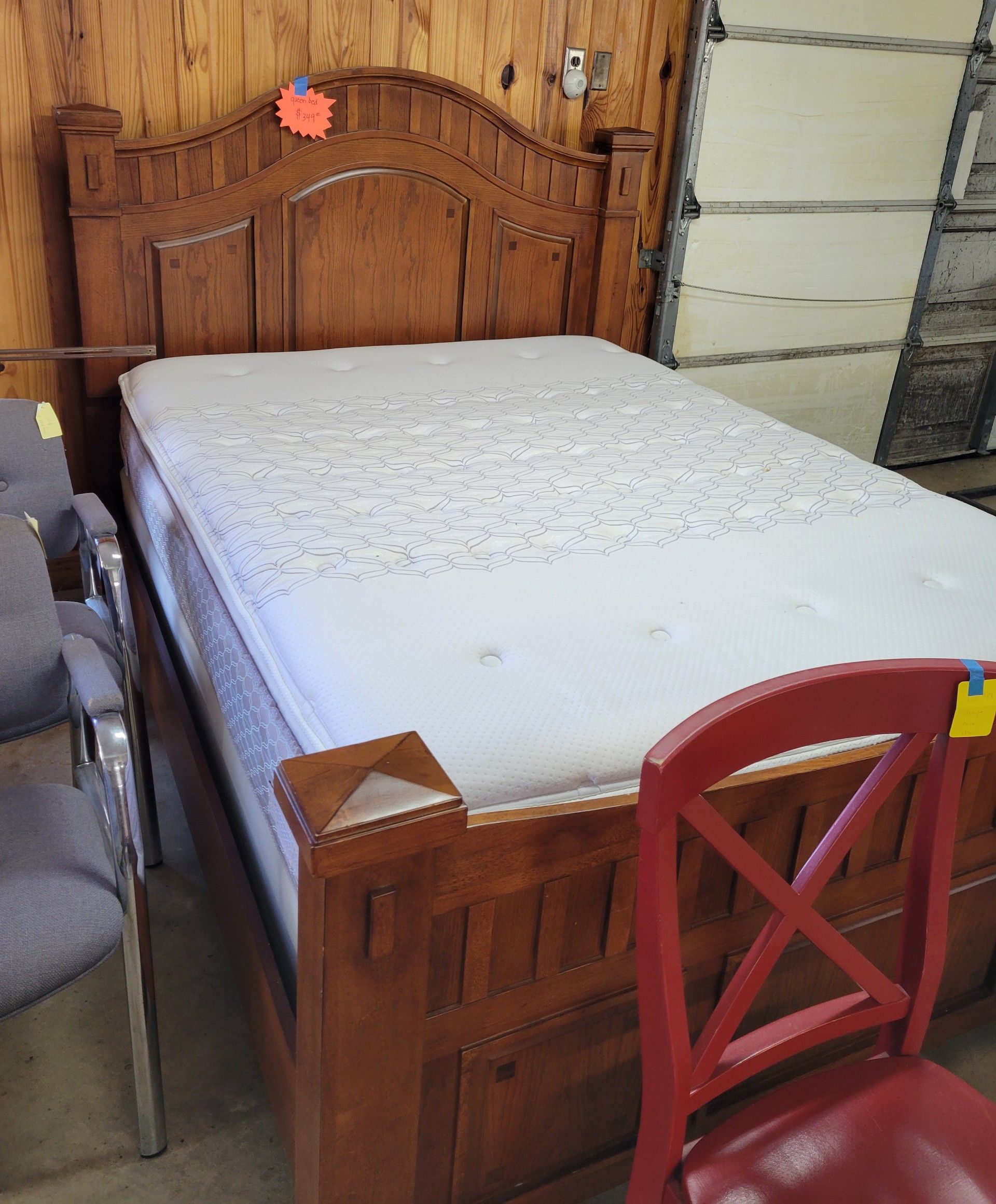 Wooden bed frame with mattress in a store setting. A red chair is in front.