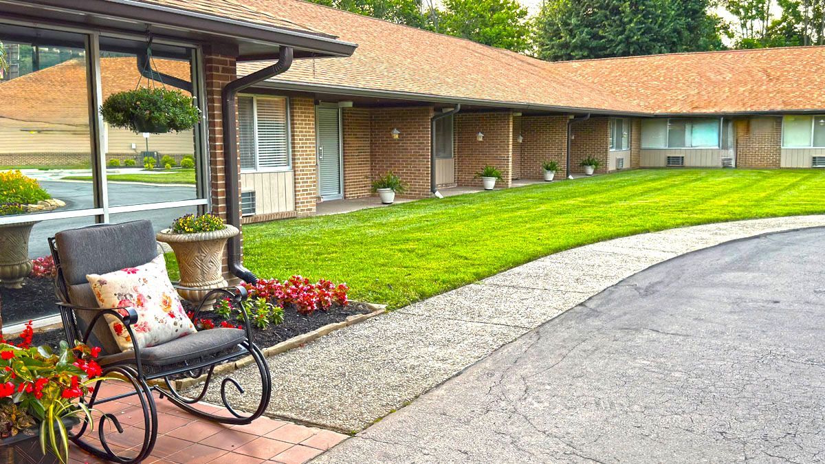 A rocking chair is sitting on the sidewalk in front of a house.
