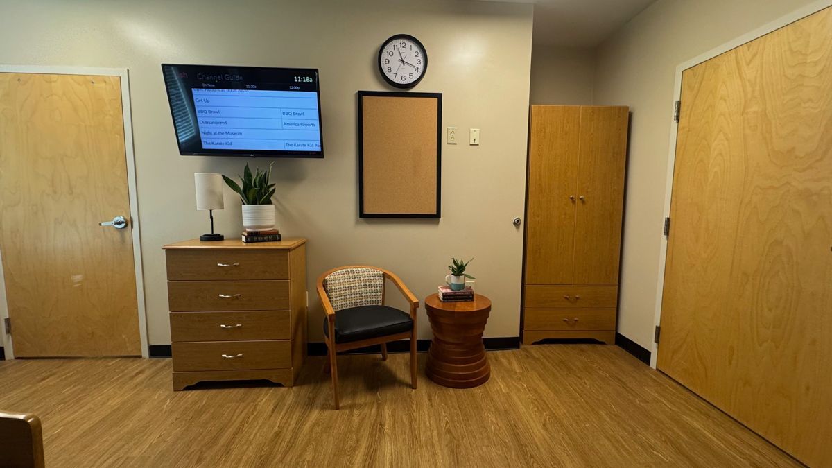 A room with a chair , dresser , television and clock on the wall.