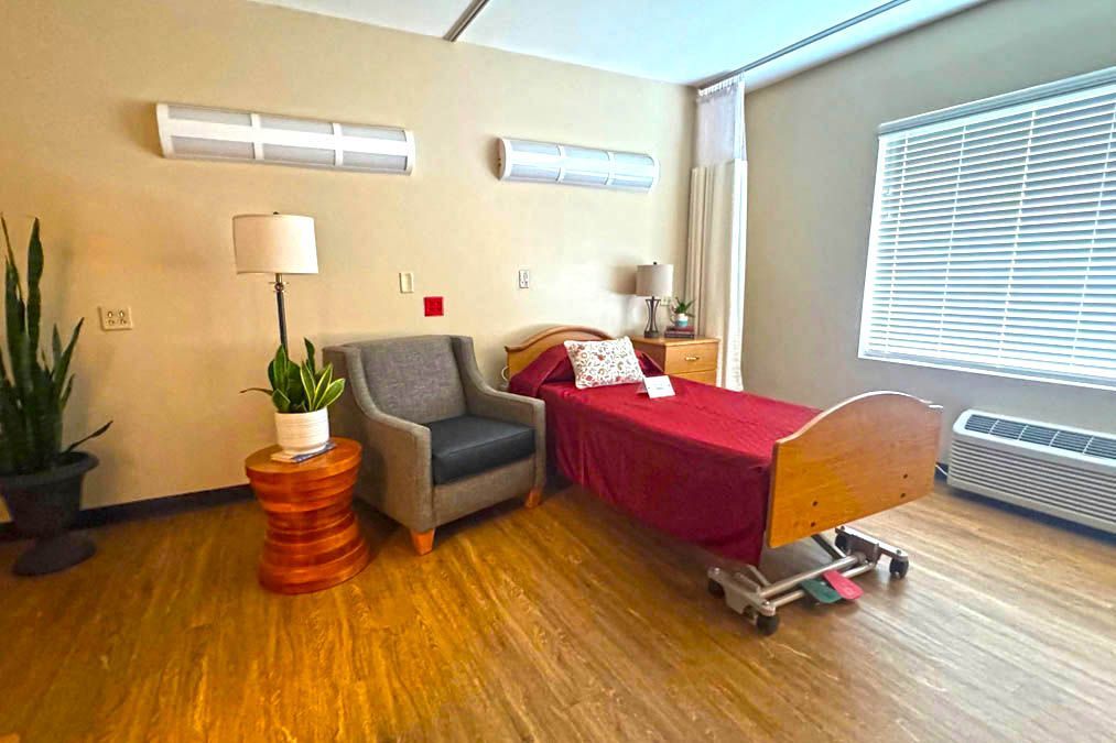 A hospital room with a bed , chair , lamp and window.