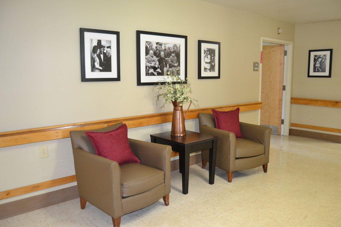 Two chairs and a table in a hallway with pictures on the wall