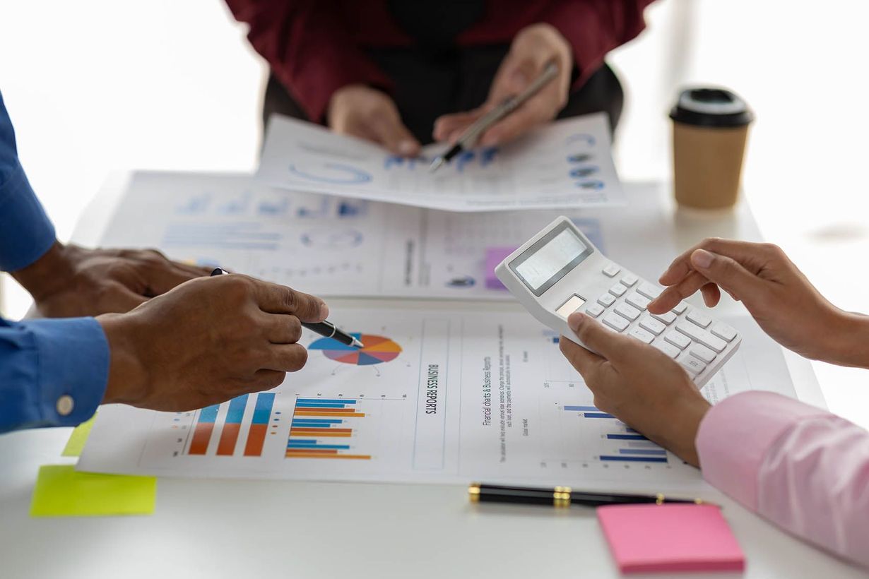 A group of people are sitting around a table looking at graphs and using a calculator.