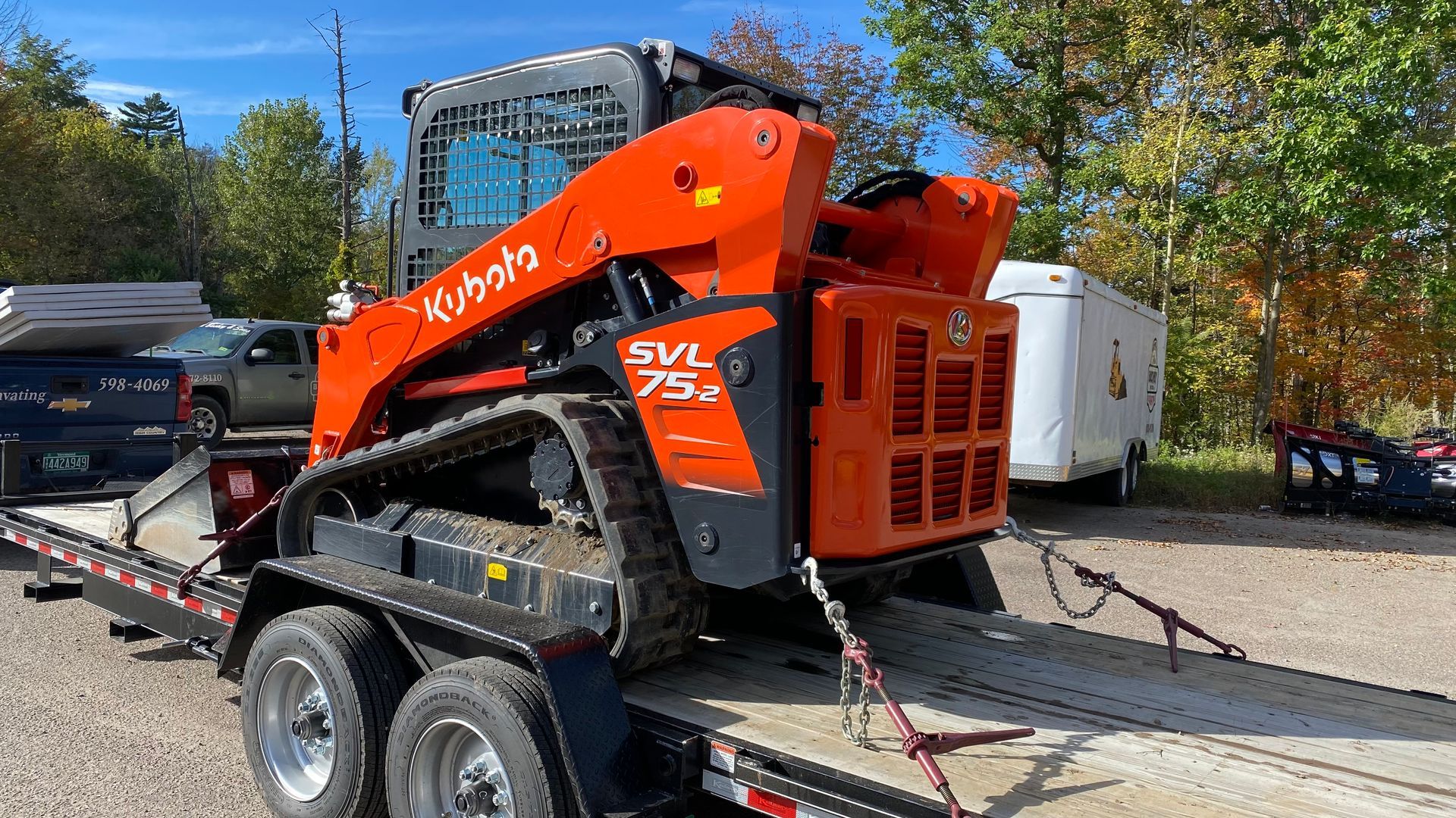 Orange Kubota SVL75 skid steer on a trailer in a parking lot under a blue sky.