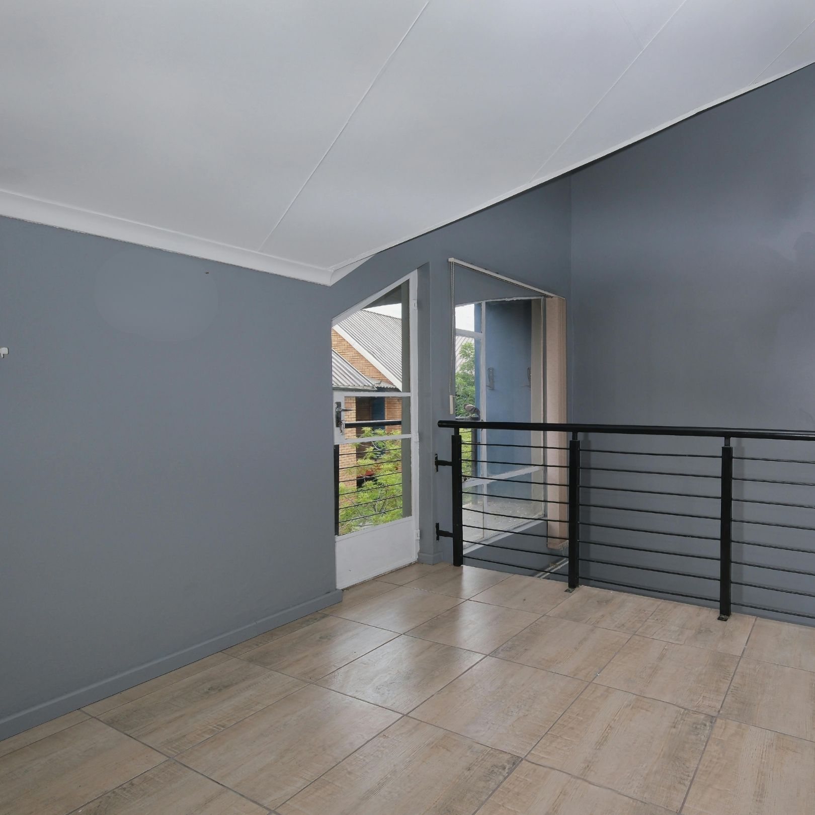 A room with light wood-look tile floors, gray walls, a white ceiling, a glass-paned door, and a black metal railing.