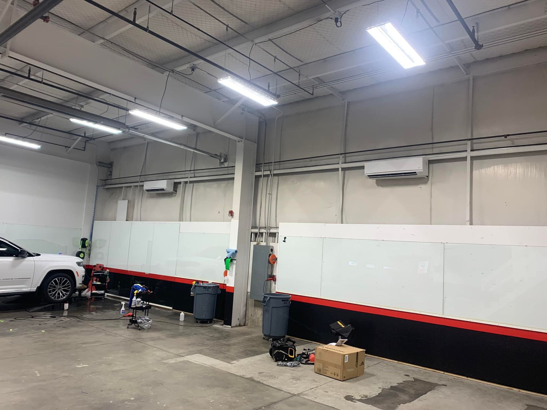 A spacious, brightly lit automotive workshop features white walls with black and red accents, tools, and a parked car.