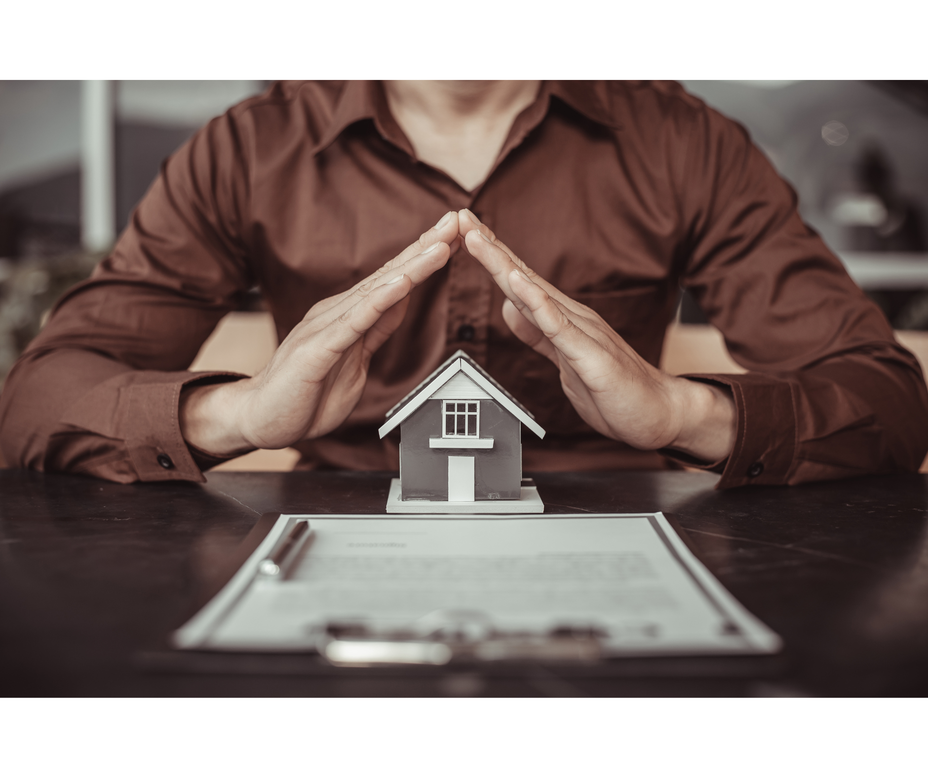 A man is sitting at a table with his hands over a model house.