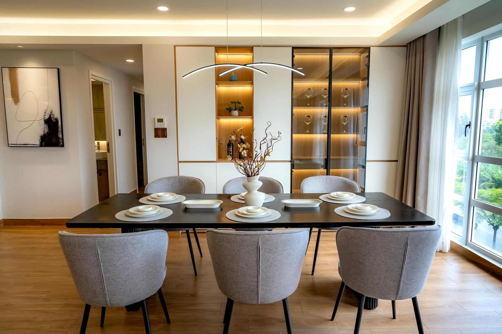 Dining room with a dark table set for six, six grey chairs, and a built-in display cabinet.