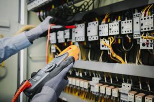 An electrician is working on an electrical panel with a multimeter.