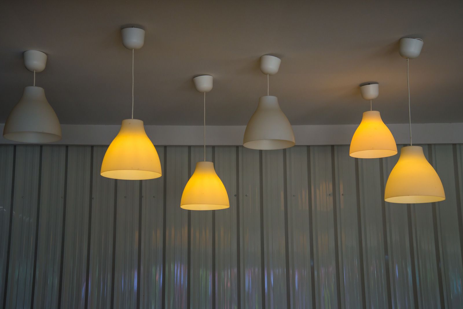 Ceiling lights, seven white pendant lamps illuminating a room, against a wood-paneled wall.