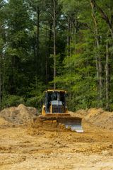 Yellow bulldozer pushing dirt in a clearing surrounded by trees.