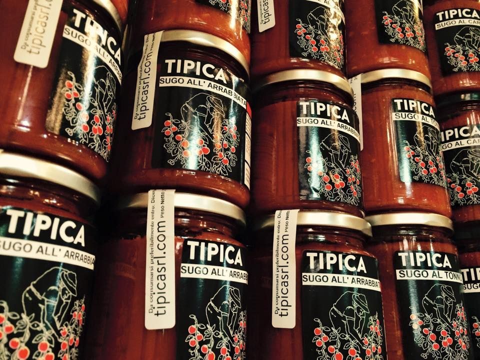 Barattoli di salsa di pomodoro del marchio Tipica impilati, etichette visibili con testo e disegno di bacche.