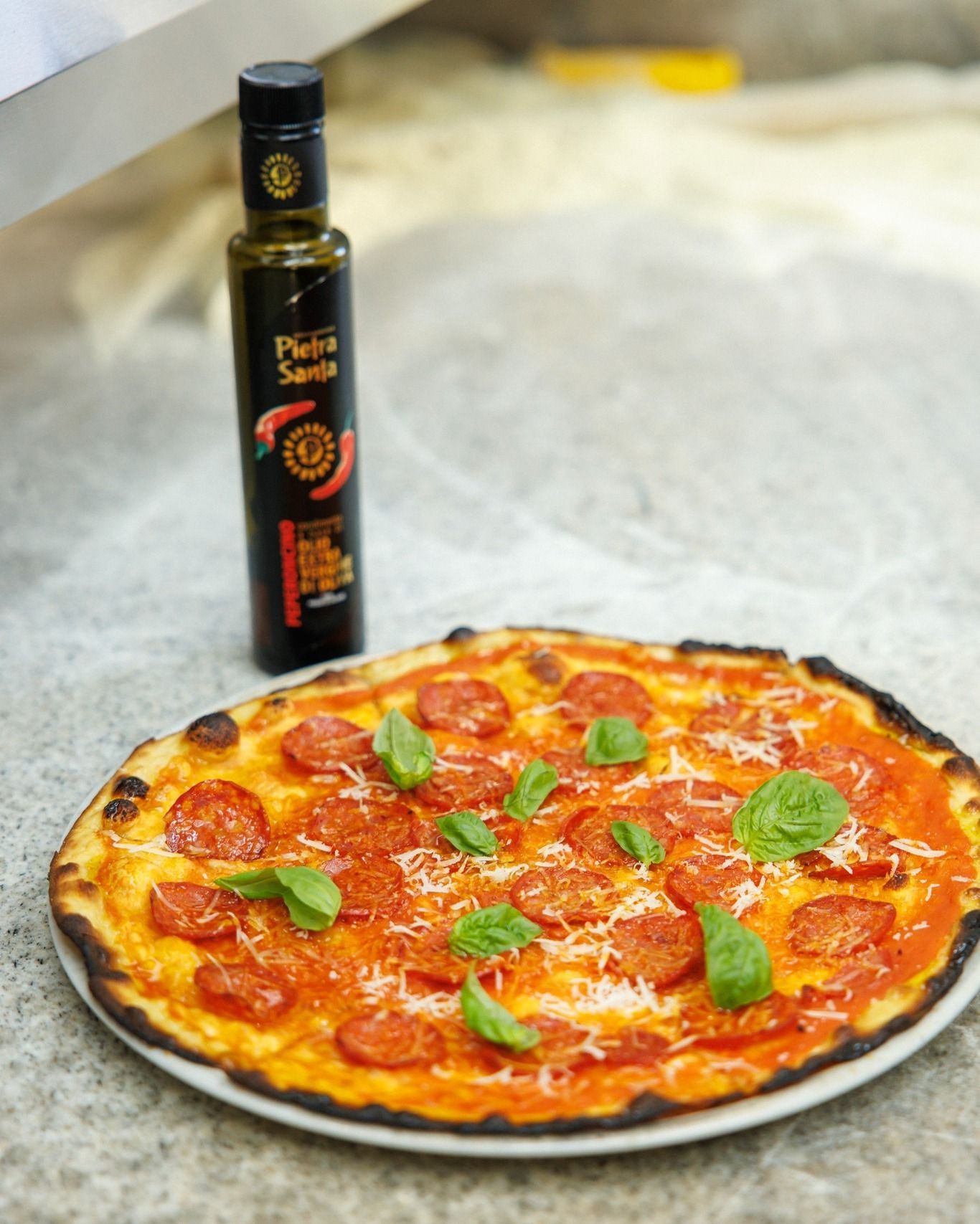 Pizza al pepperoni con basilico, parmigiano e una bottiglia di olio d'oliva piccante.