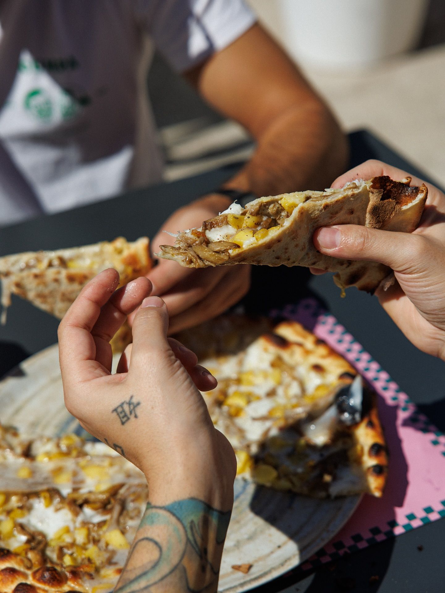 Mani che condividono una fetta di pizza all'aperto. Primo piano di mani che si tengono e mangiano.