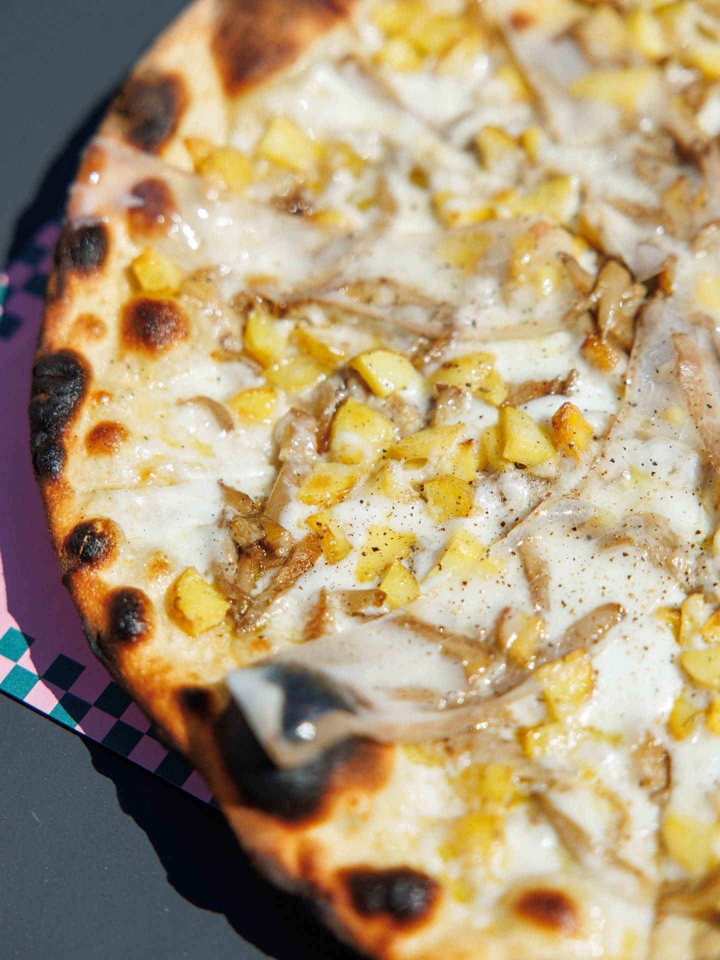 Pizza bianca con condimenti: patate a cubetti e funghi, su carta a quadretti.