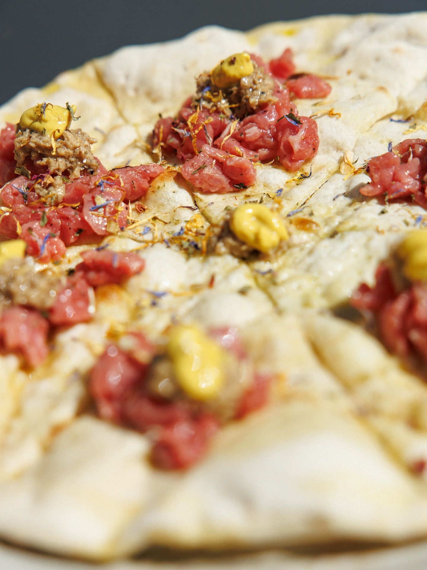 Pane piatto condito con carne cruda, cucchiaiate di senape gialla ed erbe aromatiche.