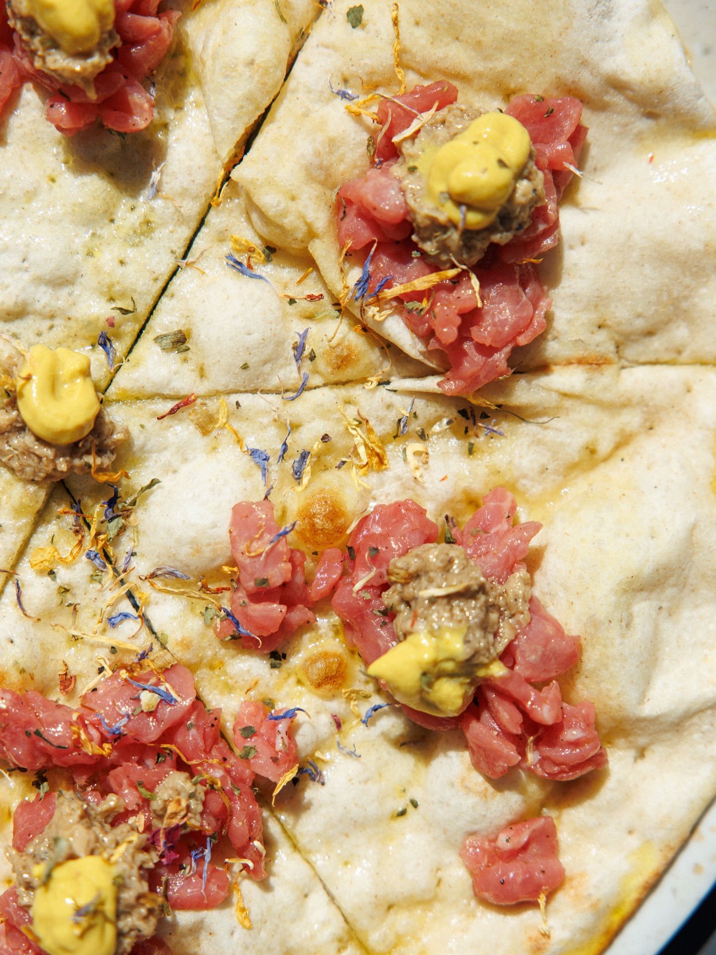 Pizza piatta con carne cruda e salsa gialla.