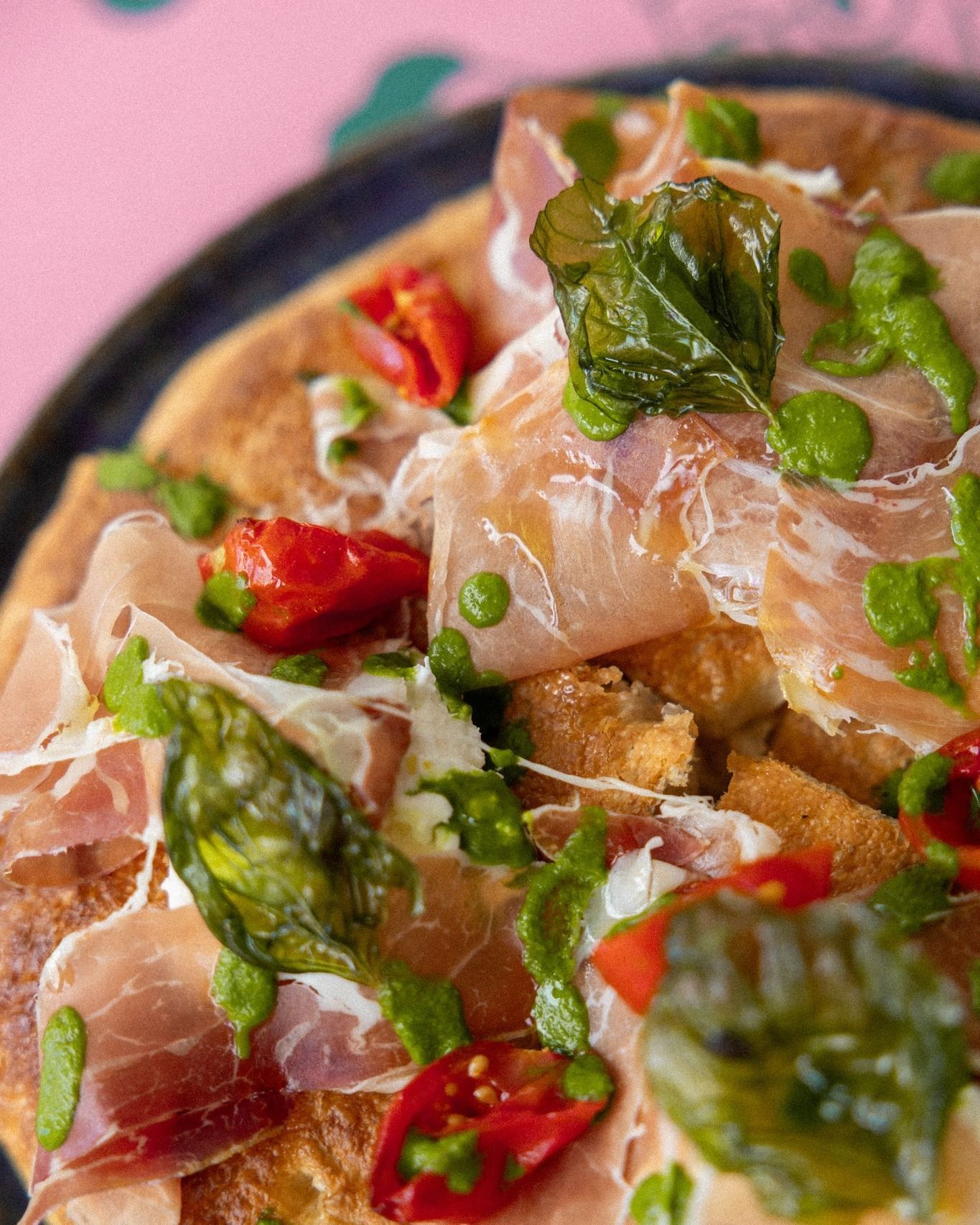 Focaccia con prosciutto, pomodori, pesto e basilico su un piatto scuro.