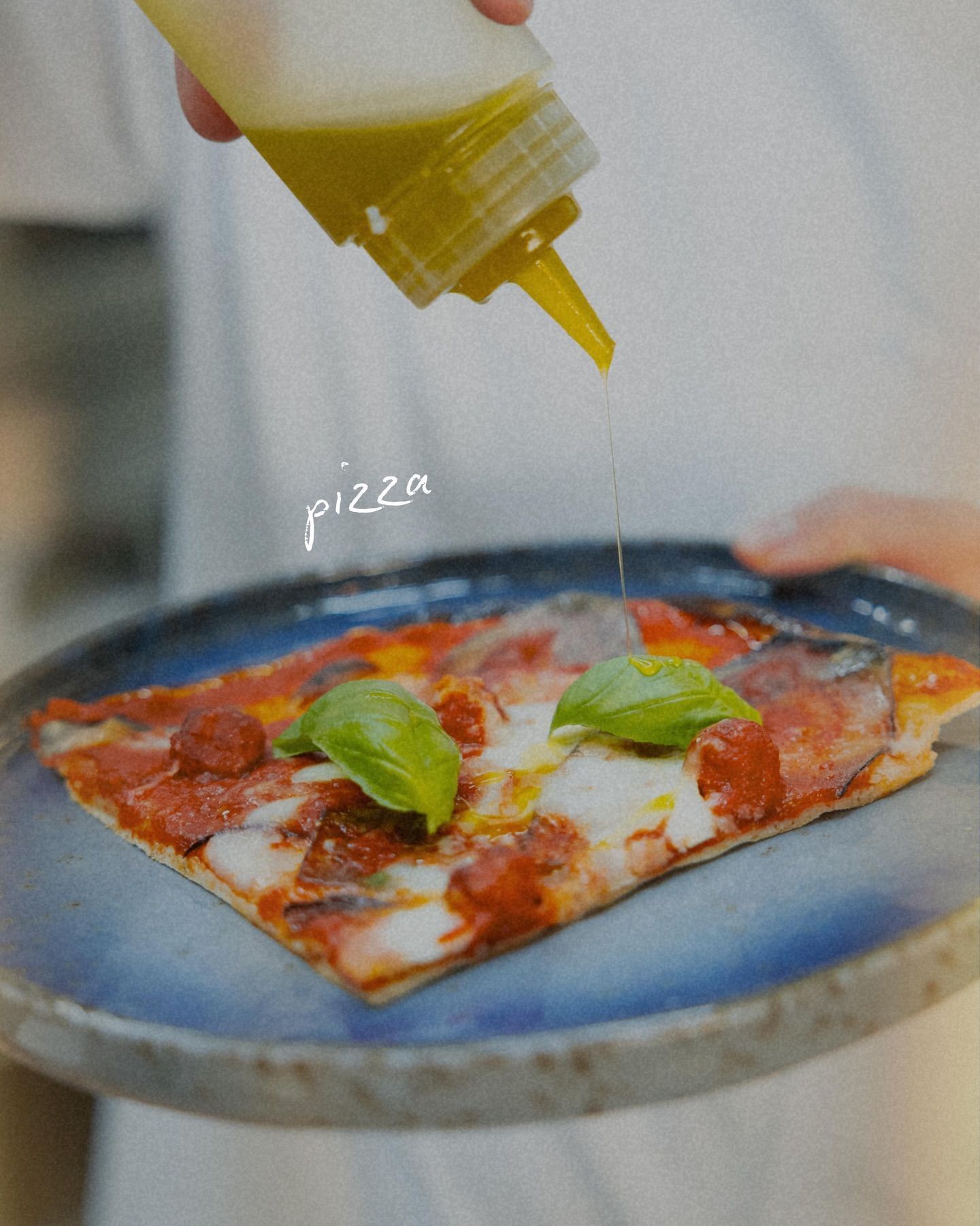 Fetta di pizza su un piatto blu, condita con olio e guarnita con basilico.