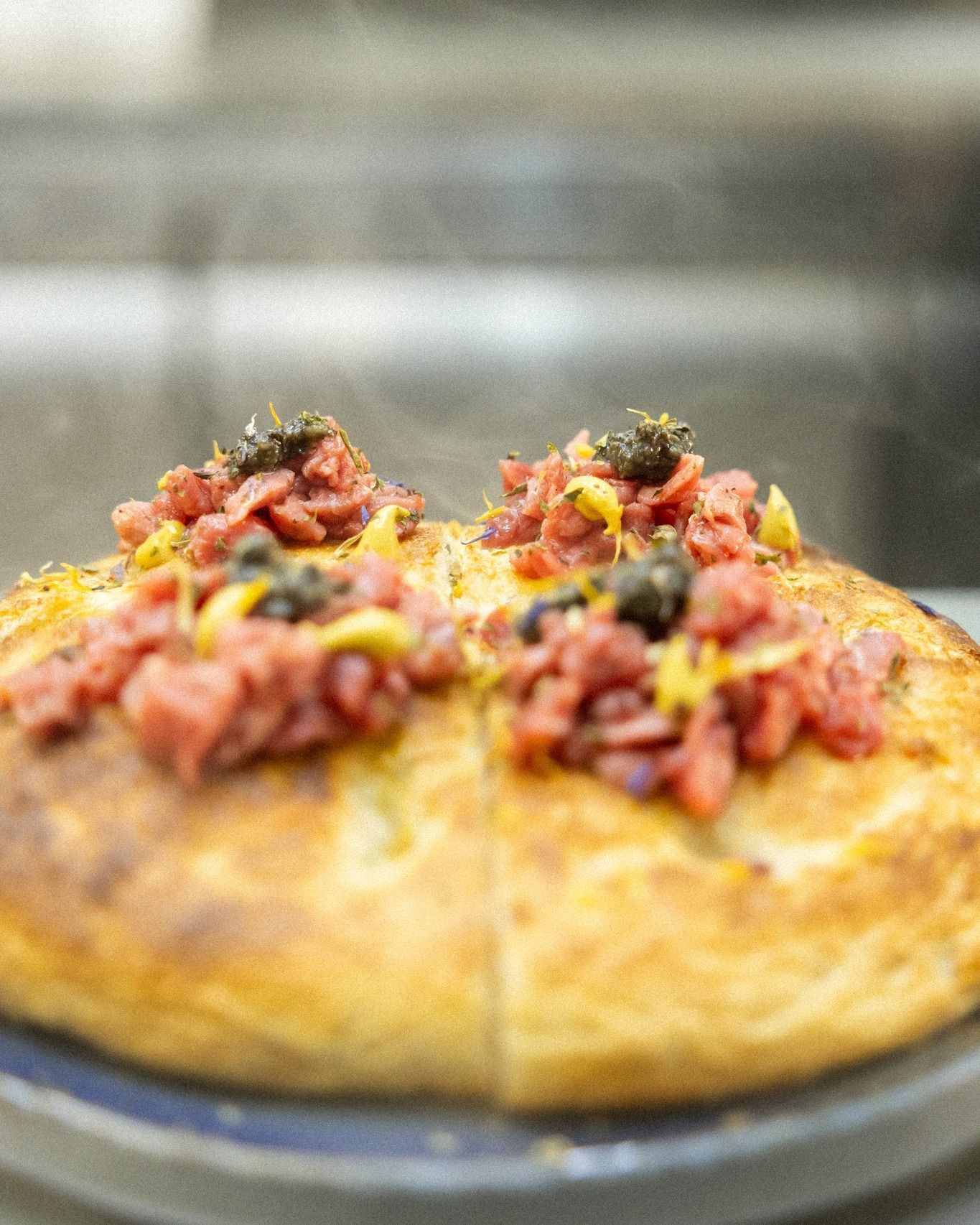 Pizza condita con carne cruda, caviale e senape.