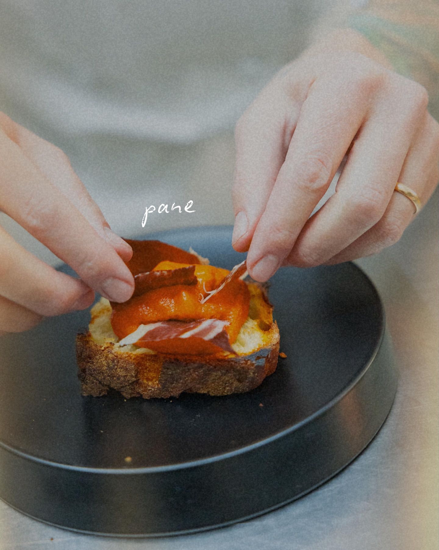 Mani che dispongono fette di carne e salsa sul pane tostato, disposto su un piatto scuro.