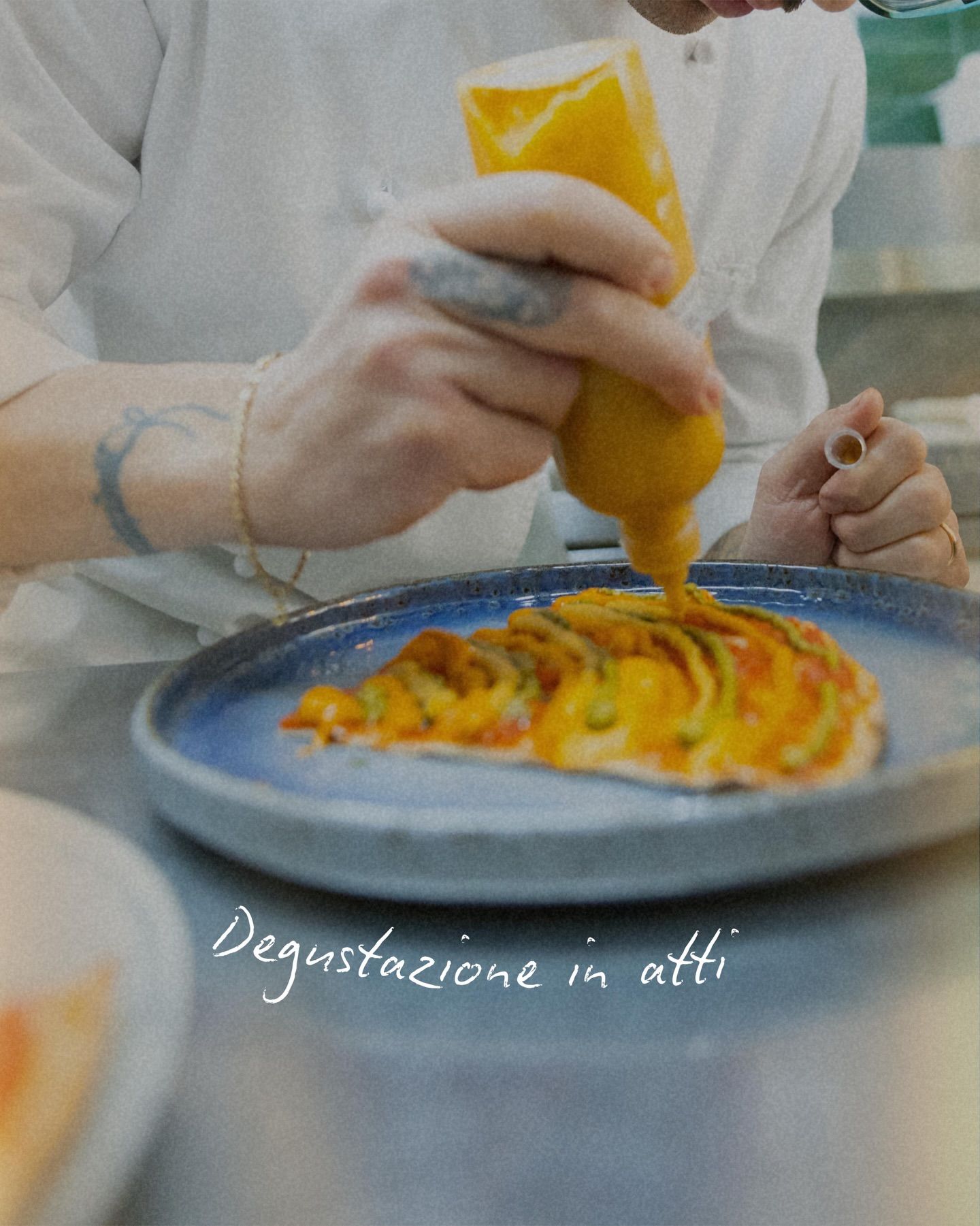 Lo chef versa la salsa gialla su un piatto, primo piano. Piatto blu, cucina luminosa.