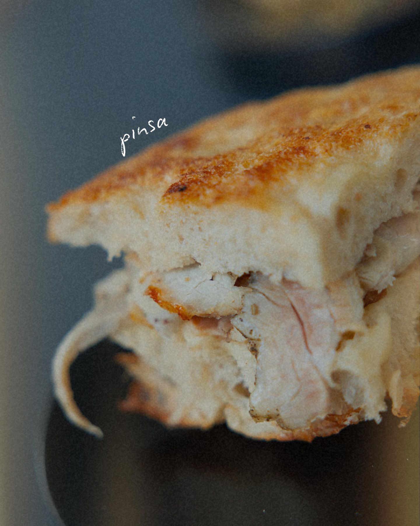 Primo piano di un panino con ripieno di pollo, pane chiaro con crosta tostata e sfondo scuro.