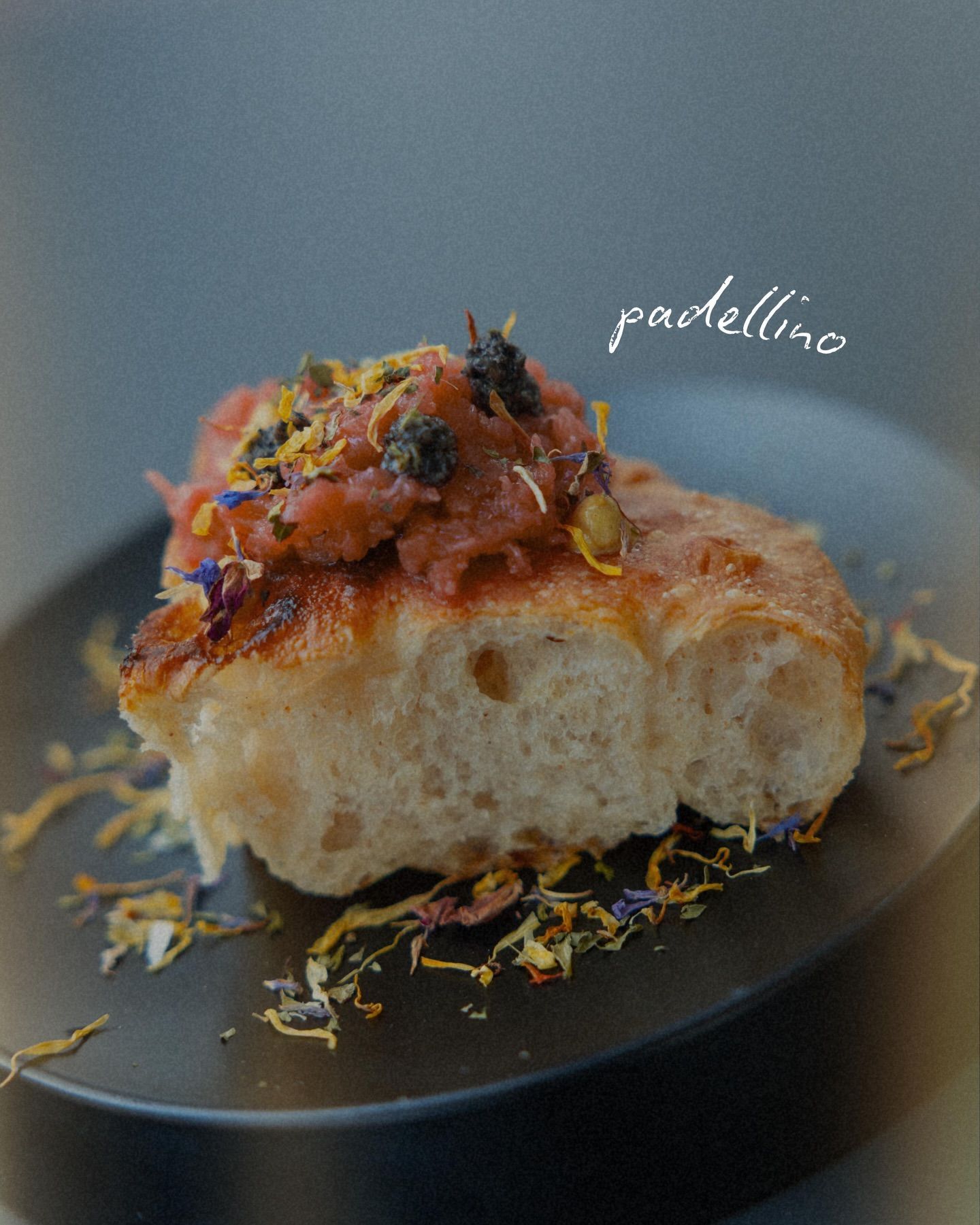 Pane tostato ricoperto di crema spalmabile rossastra, guarnito con fiori, su un piatto nero.