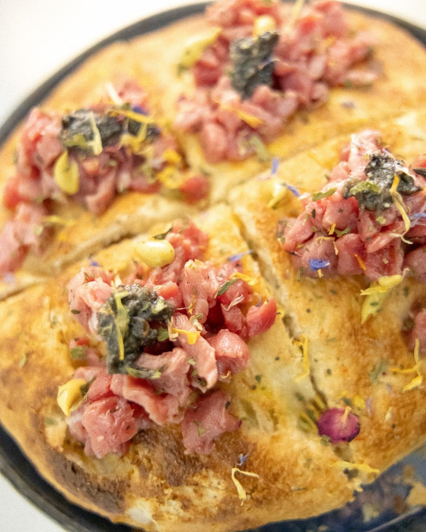 Pane rotondo condito con carne tritata, erbe aromatiche e fiori, tagliato in quarti.