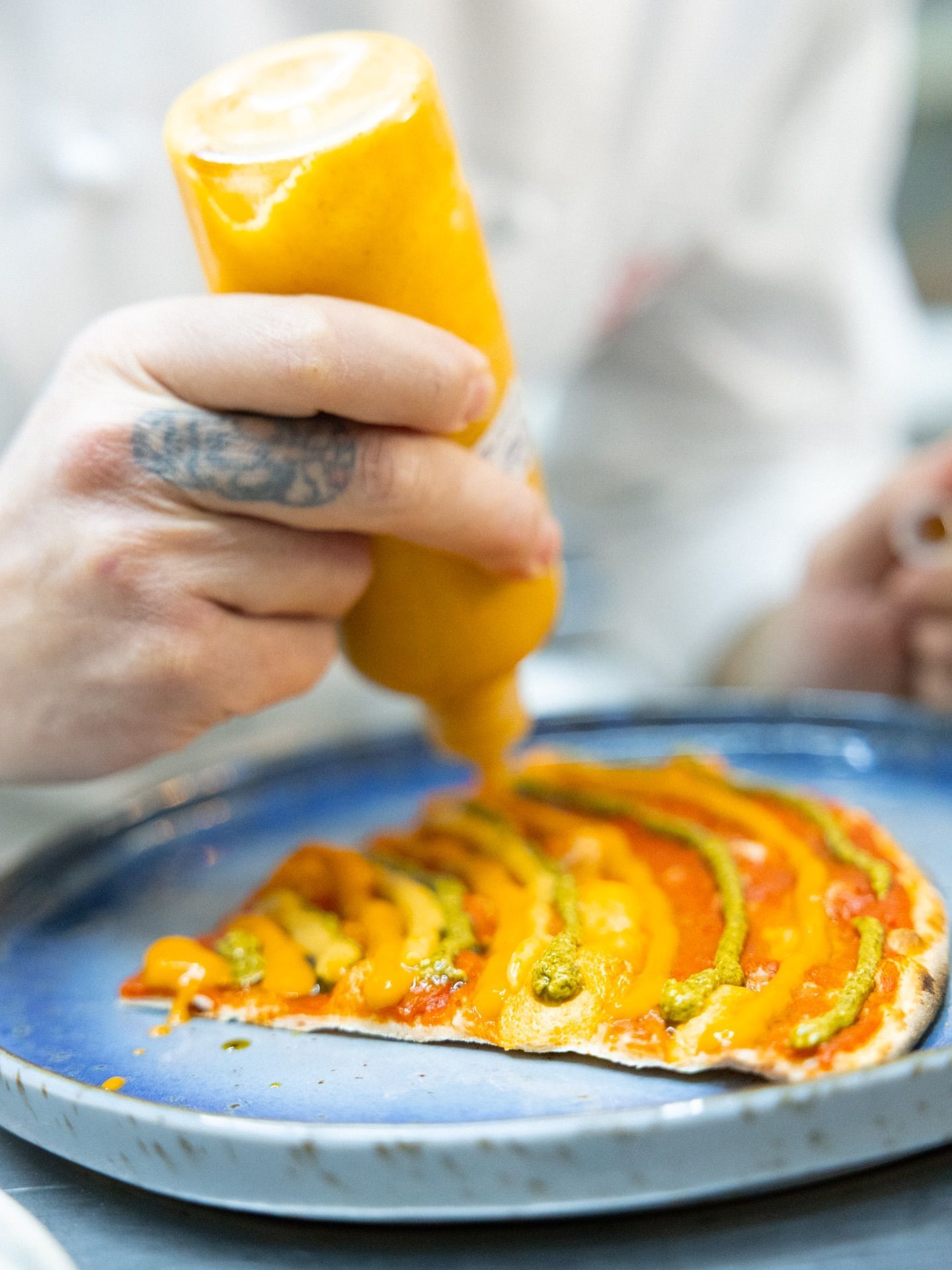 Guarnisce a mano il cibo con la salsa gialla contenuta in una bottiglia e la versa su un piatto.